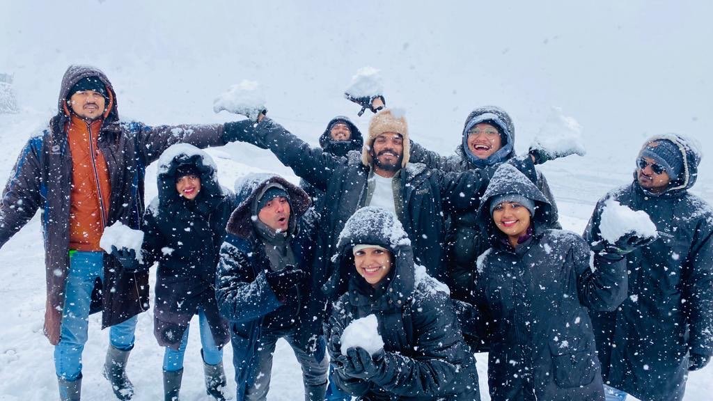 A group laughing and throwing snowballs in falling snow