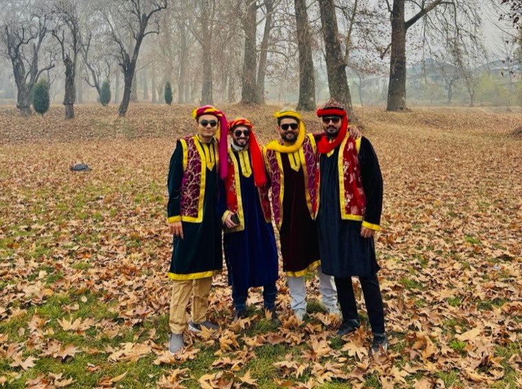 Four friends in traditional Kashmiri pherans under chinar trees